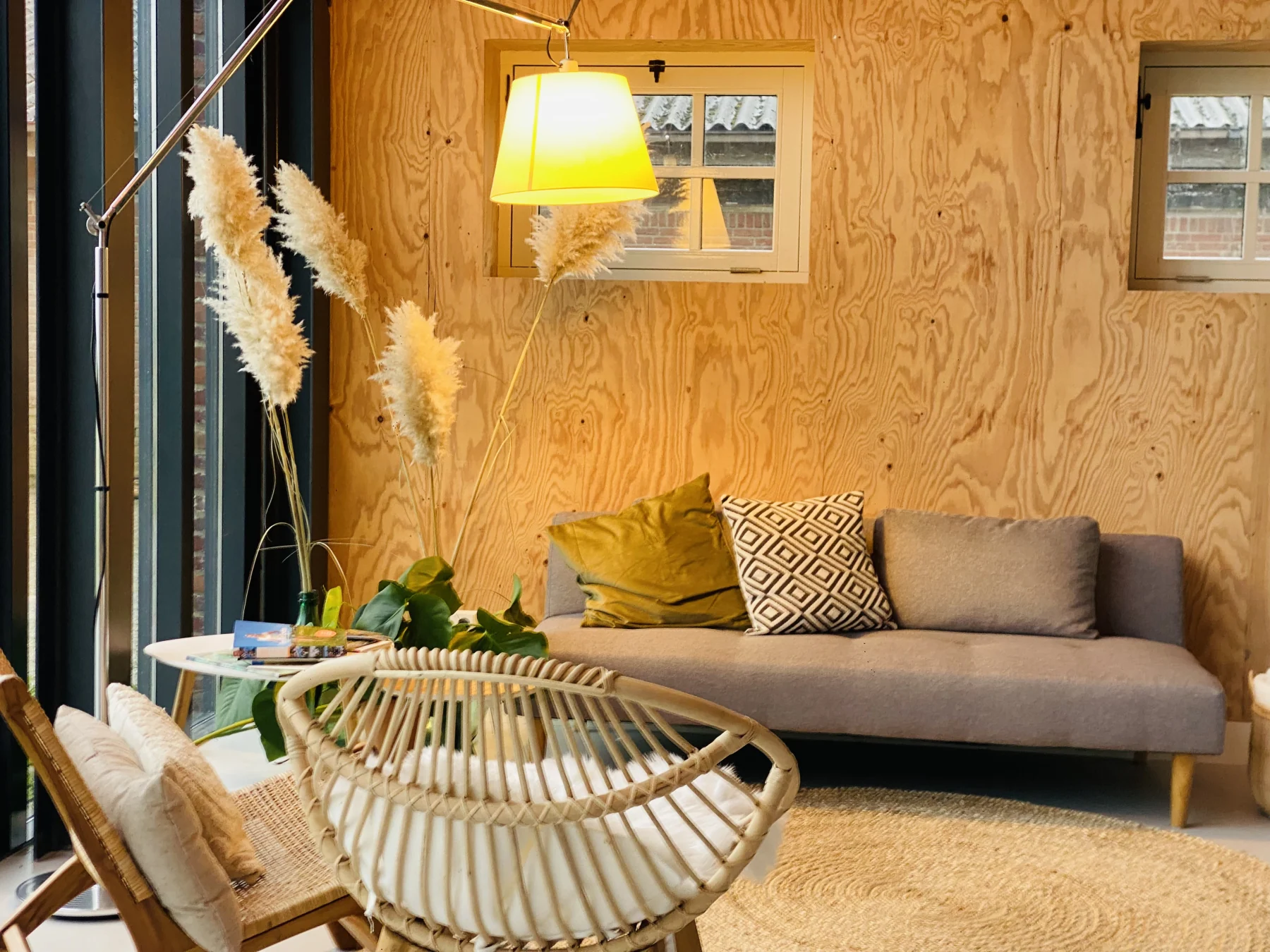 Warme zithoek met bank, rotanstoelen en verlichting bij de glazen gevel