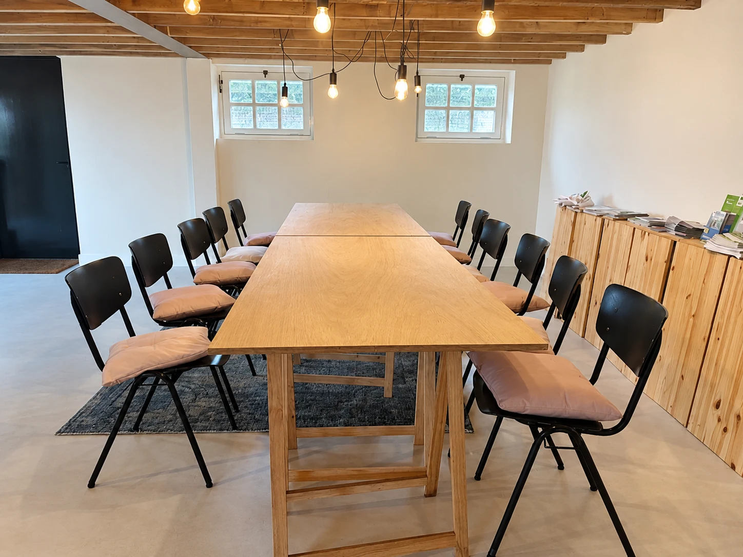 Vergaderruimte met een lange houten tafel, stoelen en warme hanglampen in De Wagenloods